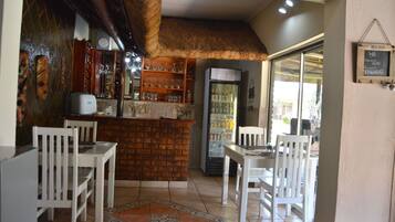 A restaurant with a brick counter, white chairs, and a refrigerator.