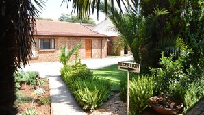 A reception area with a sign, a brick building, and a garden with various plants. - Aero Guest Lodge (Kempton Park)