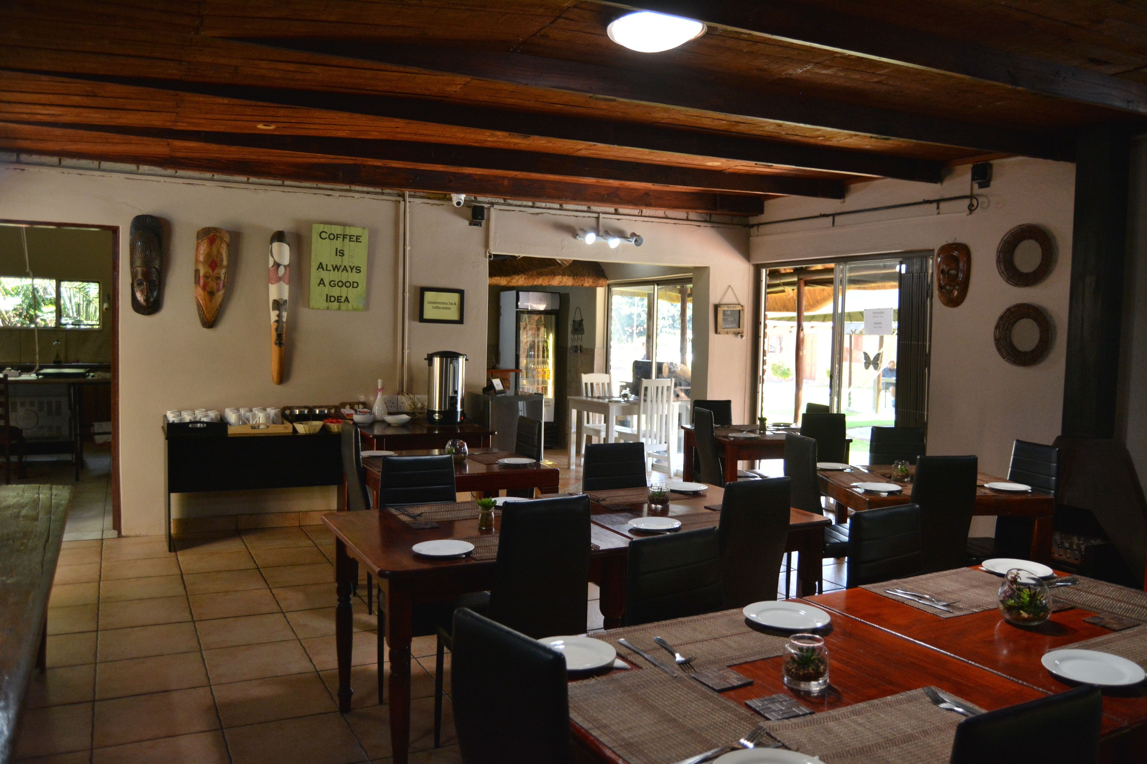 A dining area with wooden tables and chairs, a kitchen in the background, and a sign on the wall.