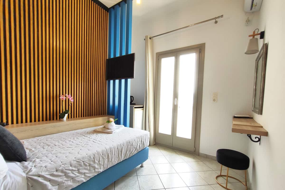 Une chambre à coucher avec un lit, un téléviseur fixé au mur, une porte donnant sur une belle vue et un petit tabouret.
