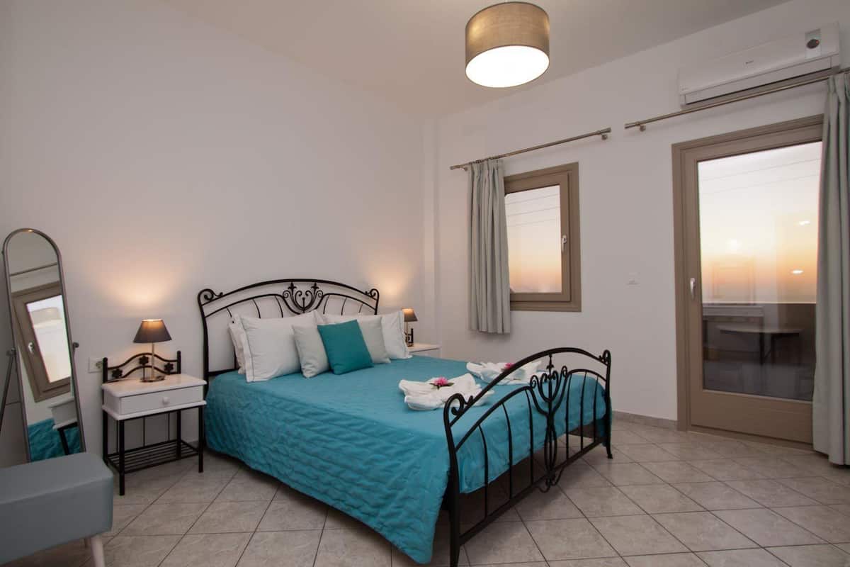 Une chambre à coucher comprenant un lit, des tables de chevet, un miroir, une fenêtre avec des rideaux et un appareil de climatisation.