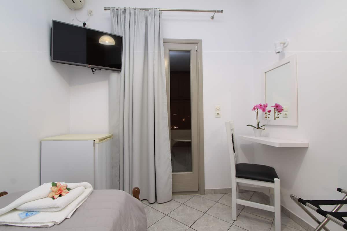 Une chambre d’hôtel avec un lit, une chaise, une télévision, un miroir et une petite étagère ornée de fleurs.