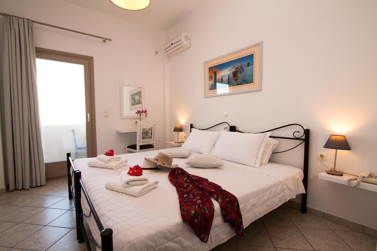 Une chambre d’hôtel avec un lit, des lampes de chevet, un tableau, une chaise et une fenêtre avec des rideaux.