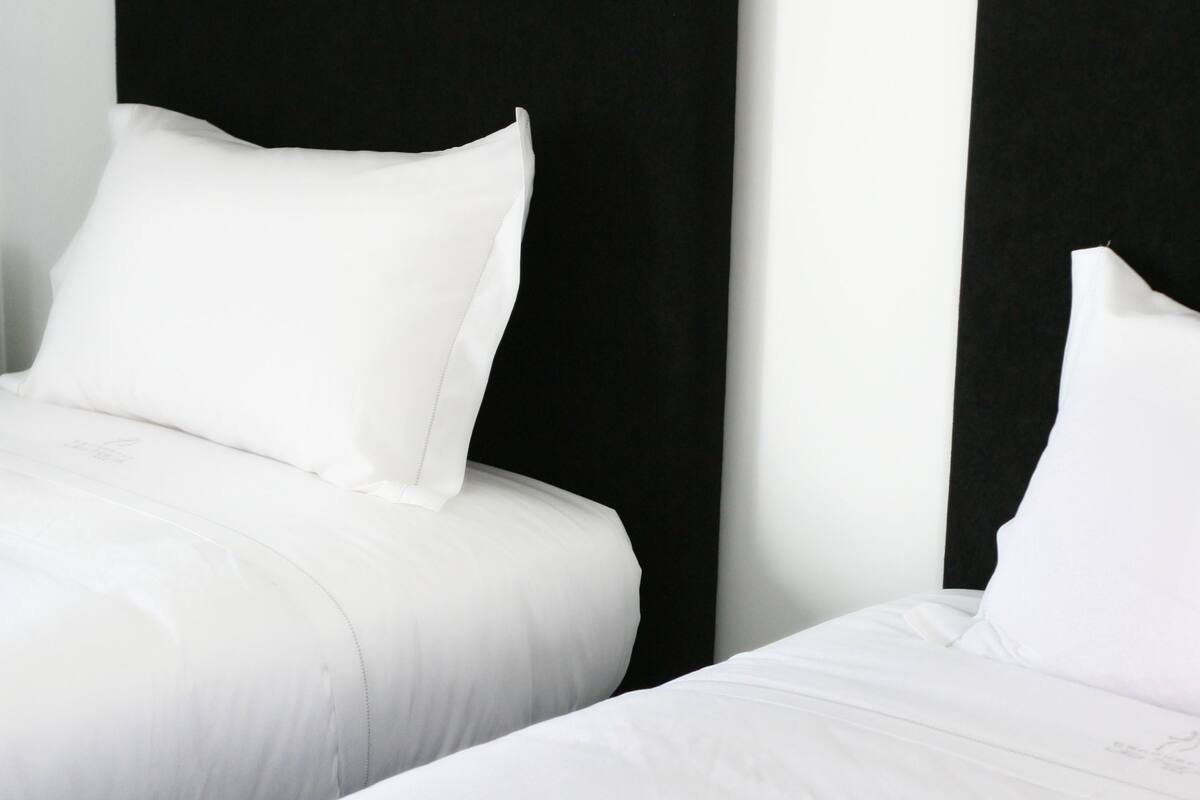 Dos camas con cabeceros negros y ropa de cama blanca.