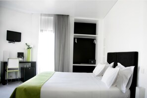 A modern hotel room with a bed, a desk with a chair, a TV, a wardrobe, and a window with curtains. - Benavente Vila Hotel (Benavente)