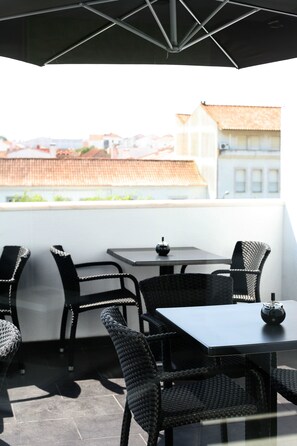 A terrace with wicker furniture, a table, and a view of buildings in the background. - Benavente Vila Hotel (Benavente)