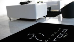 A modern living room with a black rug featuring white text, a white sofa, a black chair, and a flat-screen TV mounted on the wall. - Benavente Vila Hotel (Benavente)