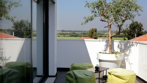 A balcony with a view of the countryside, a potted tree, and green seating. - Benavente Vila Hotel (Benavente)
