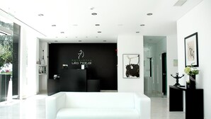 A modern hotel lobby with a white sofa, a reception desk, and a black wall with the hotel name. - Benavente Vila Hotel (Benavente)
