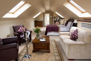 Una habitación amplia con techo alto, una cama, un sofá, un sillón y una mesa de centro.