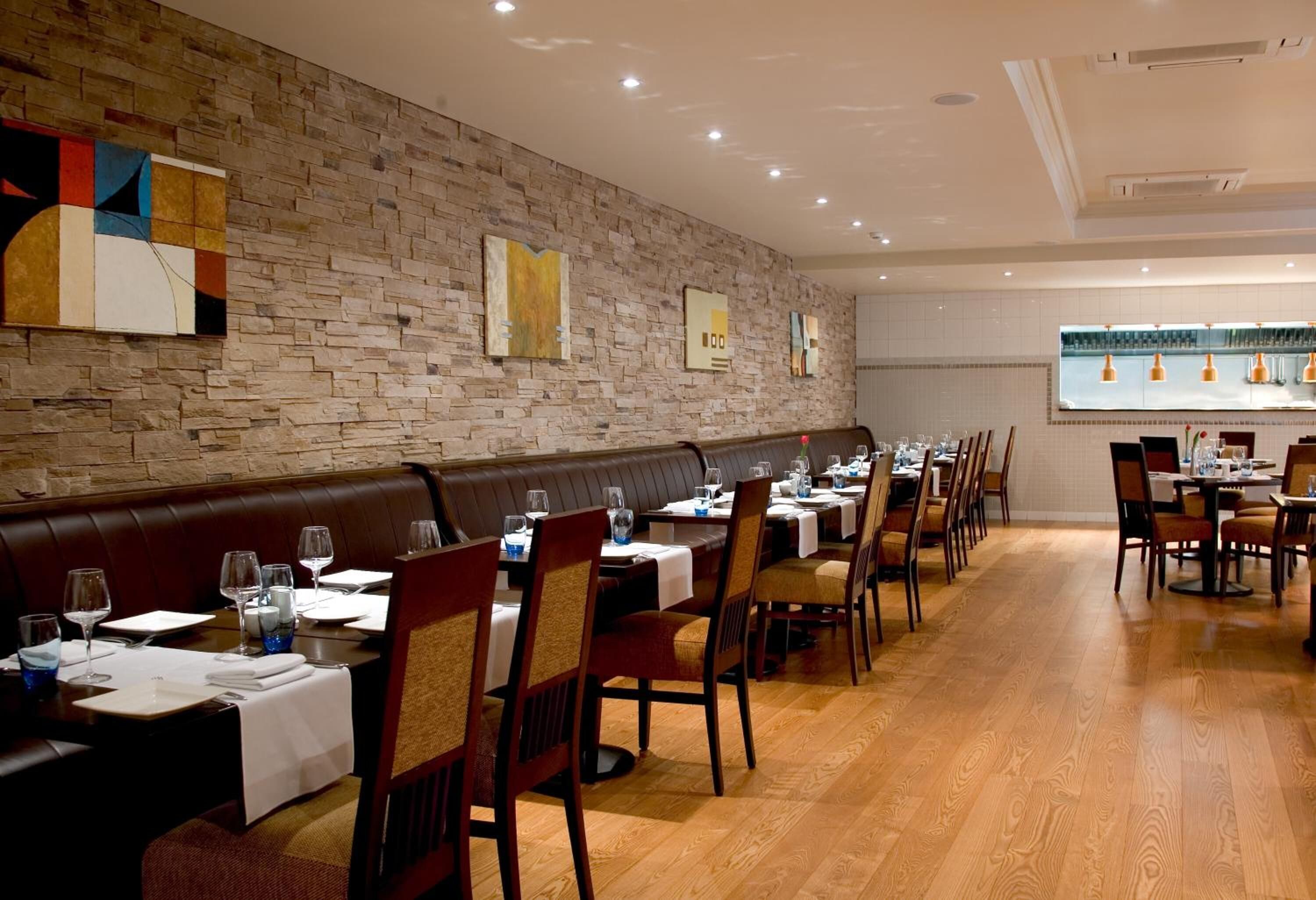 A restaurant with wooden flooring, leather booths, and tables set with white tablecloths and chairs.