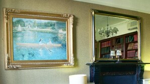 Une pièce avec une cheminée, un tableau encadré, une bibliothèque et un fauteuil à rayures.