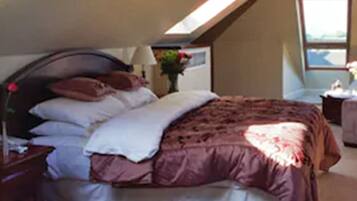 A bedroom with a sloped ceiling, a bed with a brown and white bedspread, a nightstand with a lamp, and a window with a view.