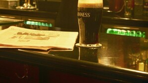 Un bar avec un verre de bière Guinness, un journal et diverses bouteilles en arrière-plan.