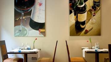 A dining area with two tables, each set with wine glasses, bottles, and a vase with a flower.