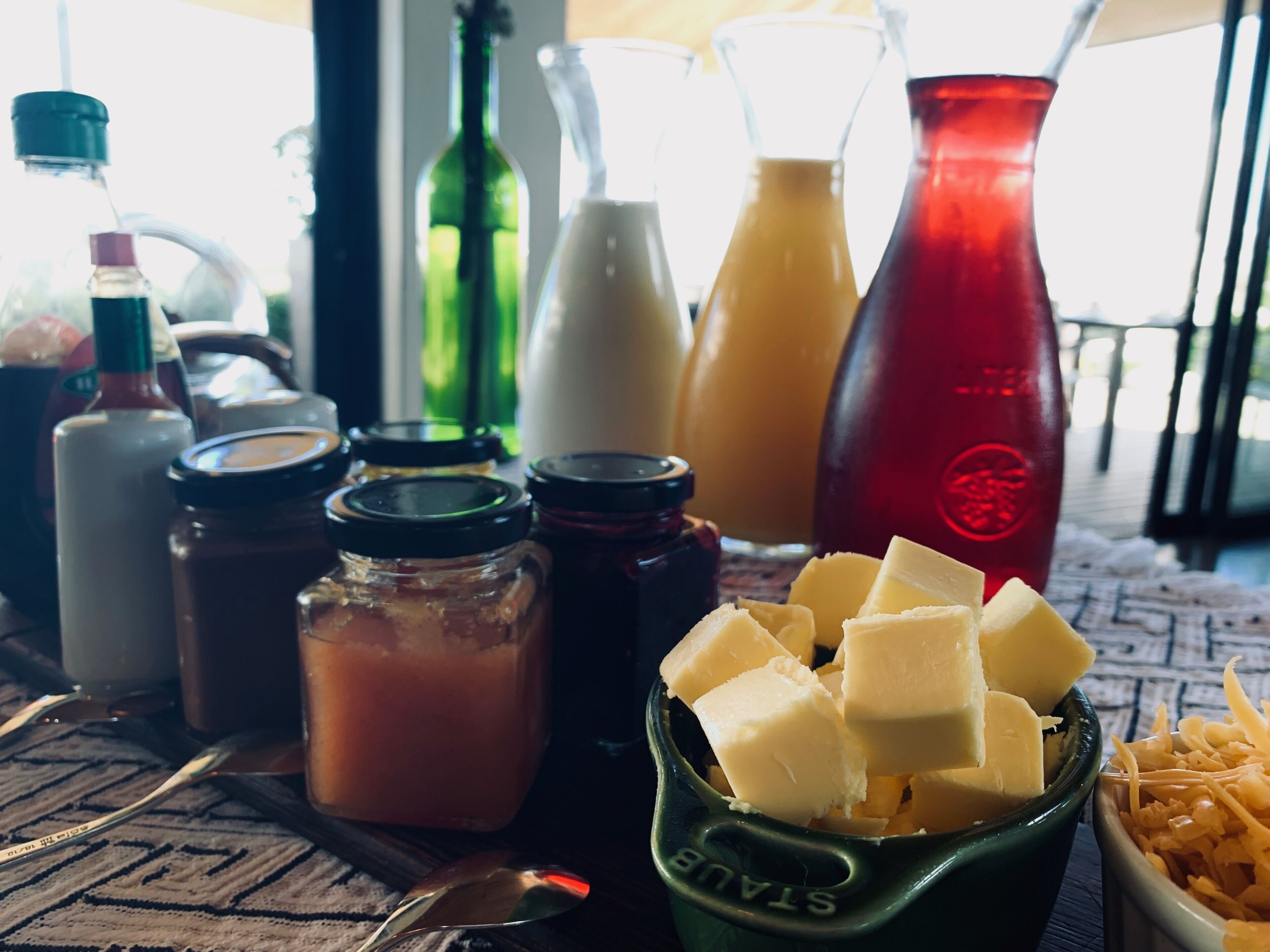 A table with various condiments, cheese, and a spoon.