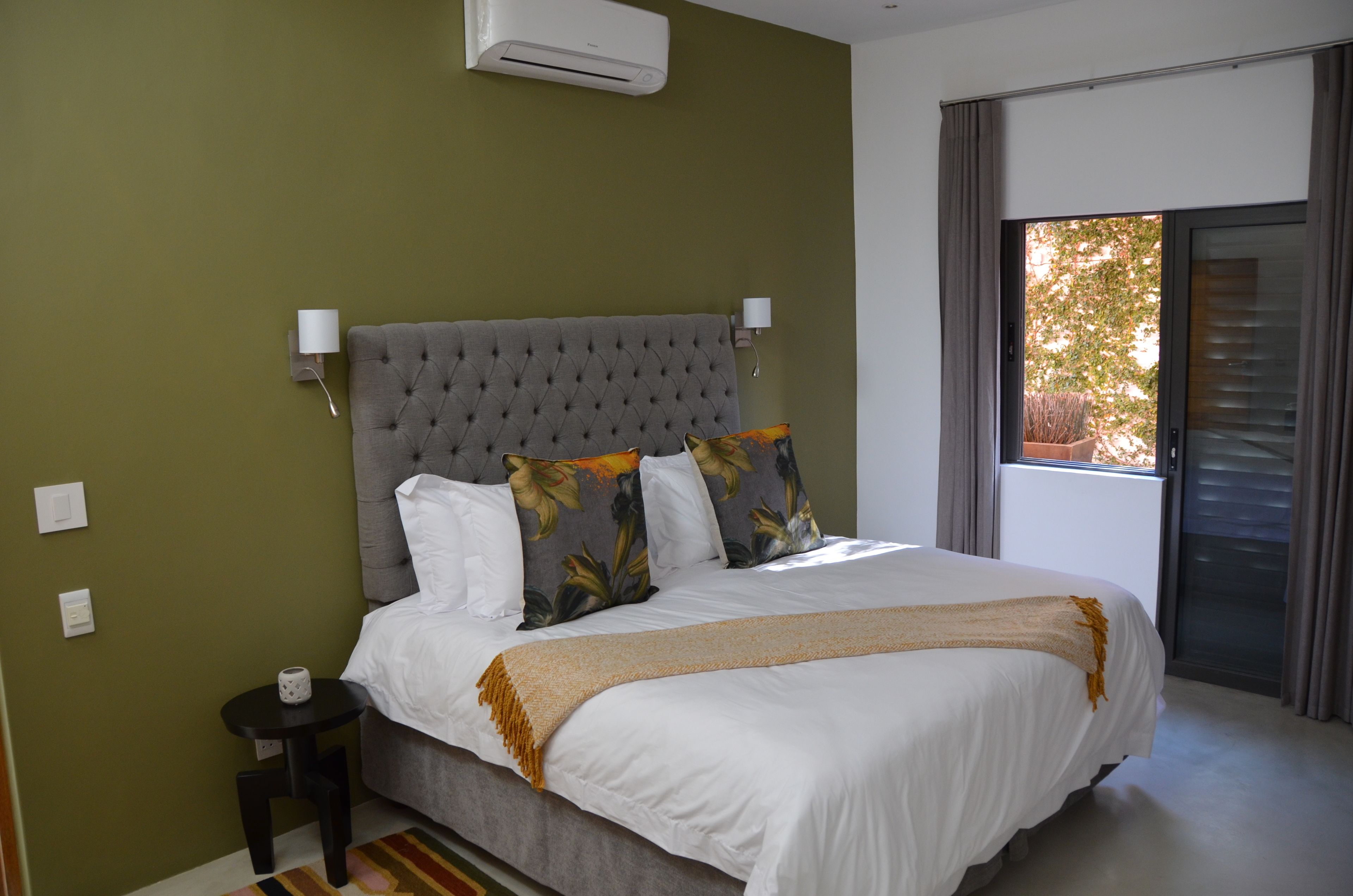 A bedroom with a large bed, a grey tufted headboard, white bedding, and a window with curtains.