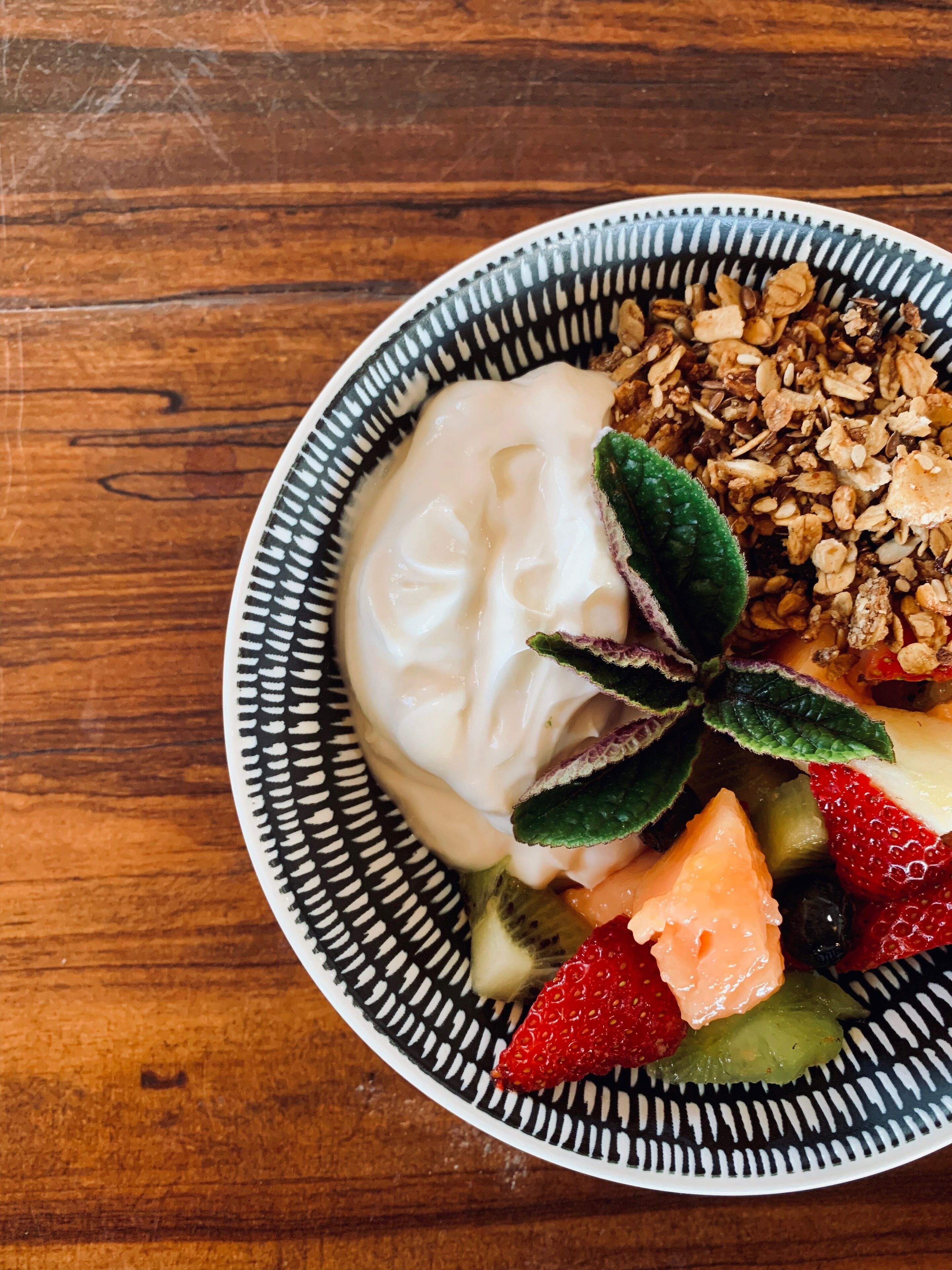A bowl of yogurt with granola and fresh fruits on a wooden table.
