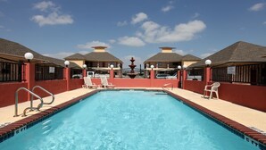 Una piscina rettangolare con acqua cristallina e blu, circondata da pareti rosse e da un solarium piastrellato.