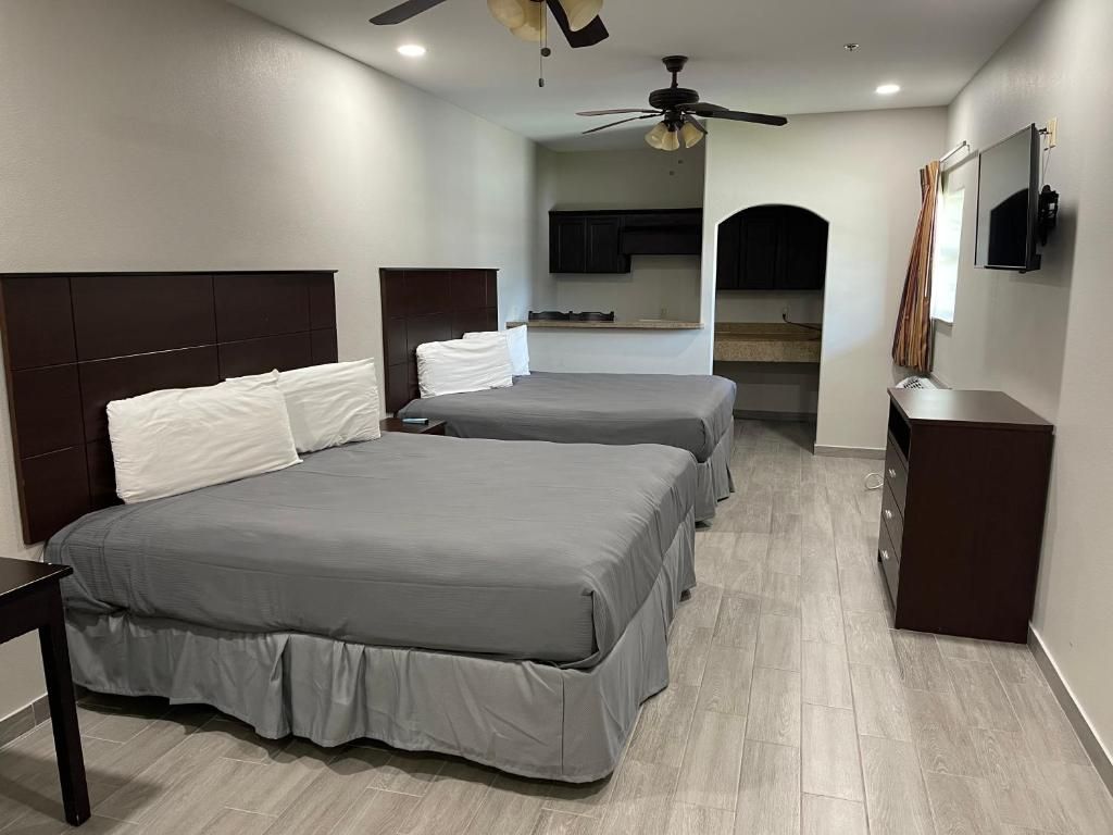 A hotel room with two beds, a ceiling fan, a kitchenette, and a TV.