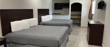 A hotel room with two beds, a ceiling fan, a kitchenette, and a TV.