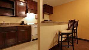 Una cucina compatta con mobili in legno scuro, un fornello bianco e un piccolo angolo bar con due sedie di legno.
