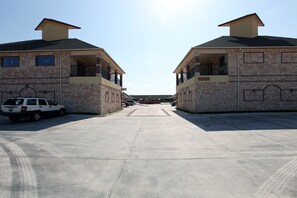 A parking lot with two brick buildings, each with a balcony and a chimney. - Guest Inn San Benito Harlingen (San Benito)