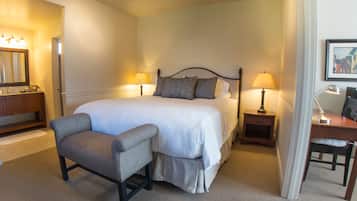 Habitación de hotel ordenada con una cama grande, lámparas de noche, una silla, un escritorio y un espejo.