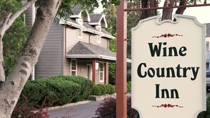 A sign for Wine Country Inn with a traditional design, surrounded by greenery and a residential building in the background. - Wine Country Inn (Jacksonville)