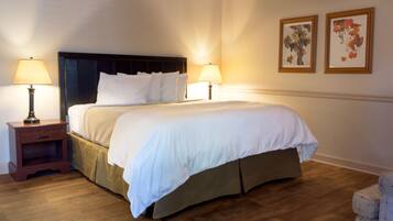 A neatly made bed with white linens, flanked by two bedside tables with lamps, in a room with wooden flooring and framed artwork on the wall.