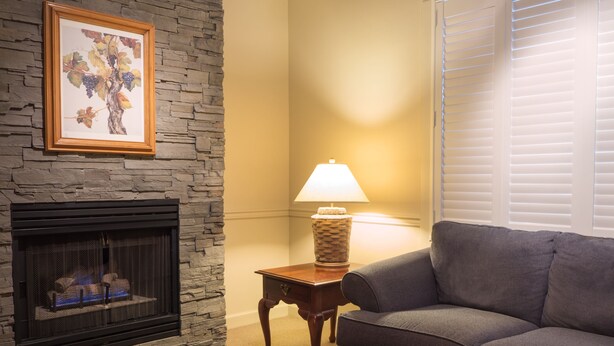 A living room with a stone fireplace, a gray sofa, a wooden coffee table, and a lamp on a side table. - Wine Country Inn (Jacksonville)