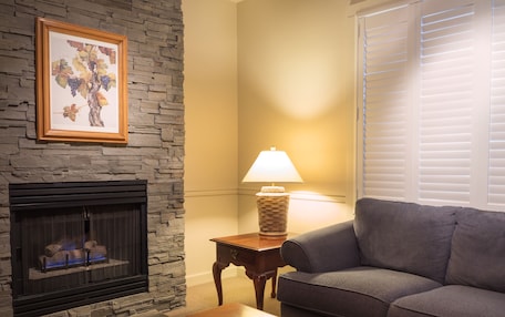 A living room with a stone fireplace, a gray sofa, a wooden coffee table, and a lamp on a side table.