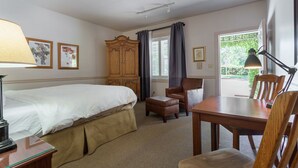 A hotel room with a bed, a wooden wardrobe, a desk with a lamp, a chair, and a dining table. - Wine Country Inn (Jacksonville)