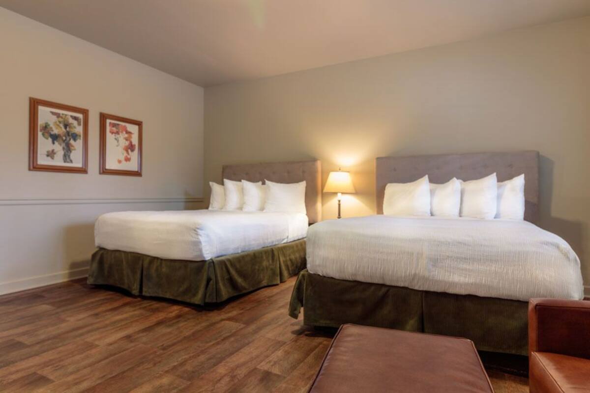 Ein Hotelzimmer mit zwei Betten, Holzboden und einem braunen Ledersessel.