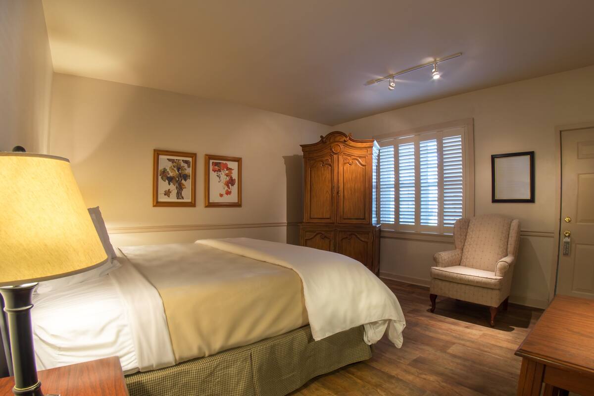 Ein Schlafzimmer mit Bett, Stuhl, Schreibtisch, Lampe und Kleiderschrank.