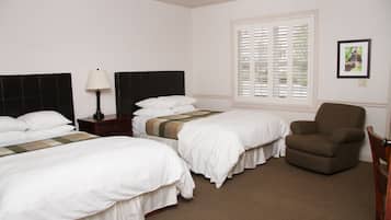 A hotel room with two beds, a nightstand, a lamp, a chair, and a window with blinds.