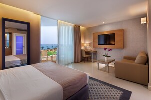 Habitación de hotel con cama, escritorio, sofá, televisor montado en la pared y vista al océano.