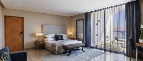Habitación de hotel con cama, mesitas de noche, escritorio, silla y vistas al exterior.