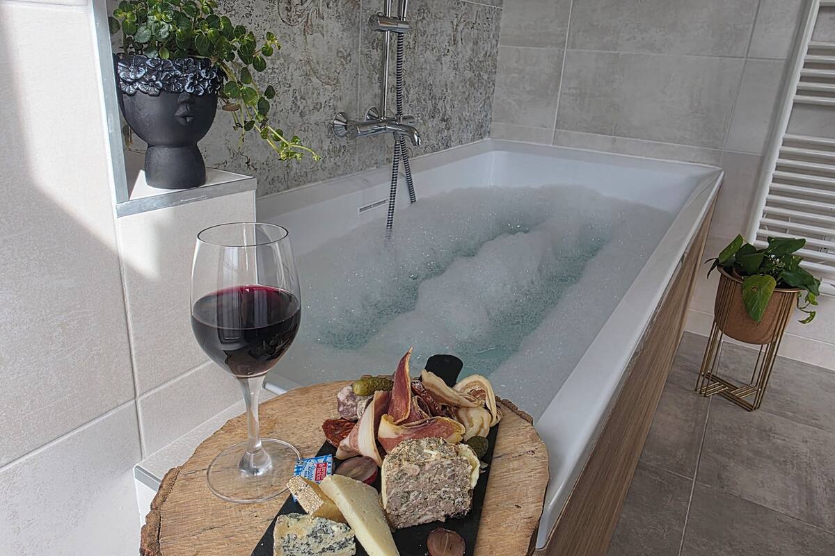 A bathtub with a glass of red wine and a charcuterie board.
