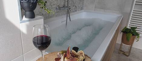 A bathtub with a glass of red wine and a charcuterie board.
