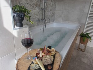 A bathtub with a glass of red wine and a charcuterie board.
