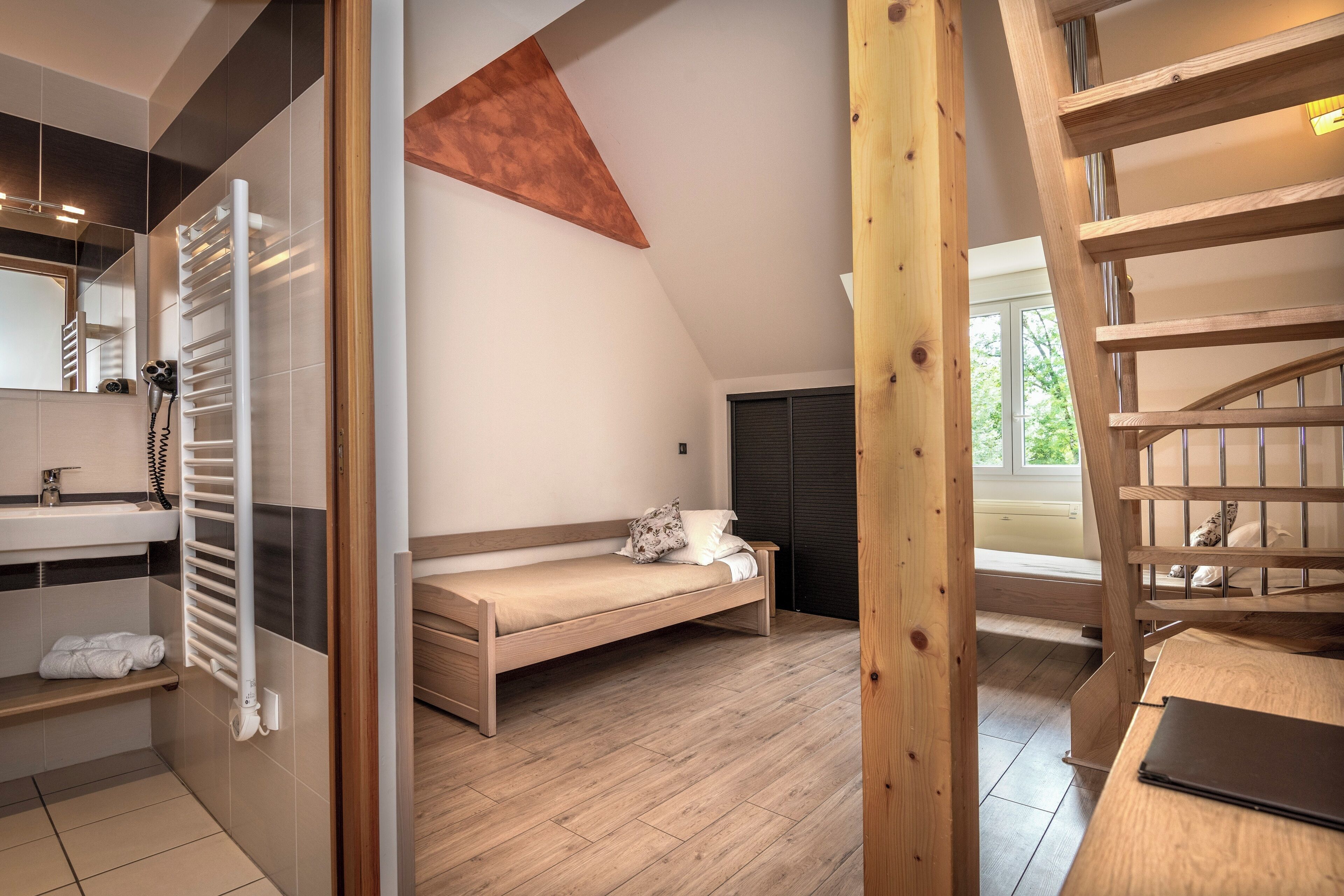 A bedroom with a wooden bed, a white bedside table, a wooden ladder, and a window with a view of greenery.