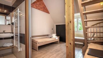 A bedroom with a wooden bed, a white bedside table, a wooden ladder, and a window with a view of greenery.