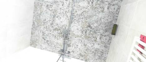 Ducha con pared de mármol, suelo de madera y bañera blanca.