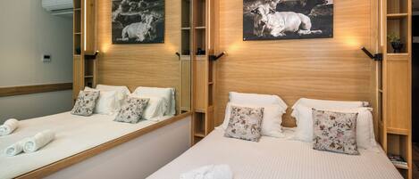 A hotel room with two beds, each with white bedding and floral pillows, a large mirror, and artwork depicting cows.