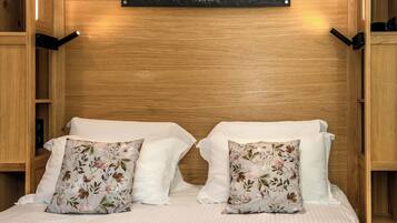 A bedroom with a wooden headboard, a framed landscape photo, and floral-patterned pillows.