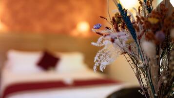 A bed with a white and red bedspread, a pillow, and a vase with dried flowers.