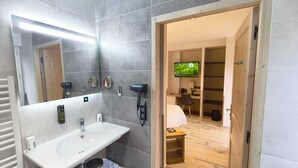 Un bany modern amb un mirall gran, un lavabo i un assecador. Hi ha una televisió a l'habitació veïna.
