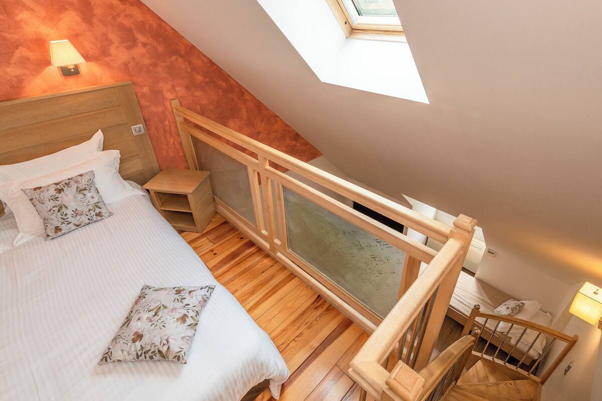 A bedroom with a bed, a nightstand, a wooden railing, and a skylight.