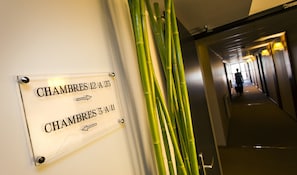 Un couloir avec des panneaux indicateurs pour les salles 12A-23 et 3A-11, et une décoration en bambou.
